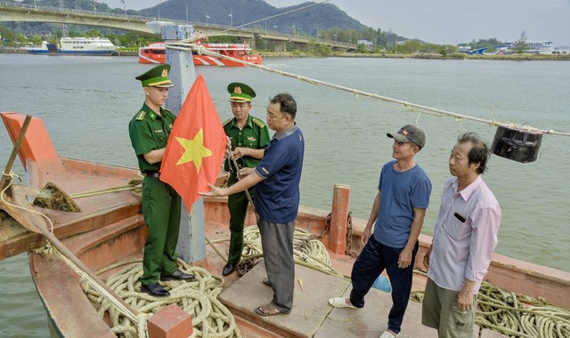 Anh Nguyễn Cao Cường đang cùng với cán bộ trạm kiểm soát Biên phòng Pháo Đài, thay lá cờ mới cho con tàu của mình trước lúc vươn khơi.